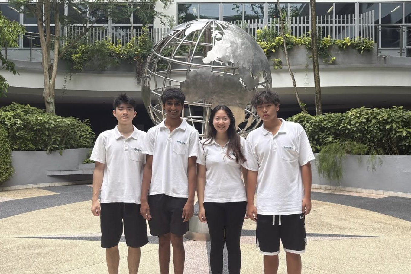 The four Dronaqua team members standing in front of the steel globe sculpture at UWCSEA Dover Campus