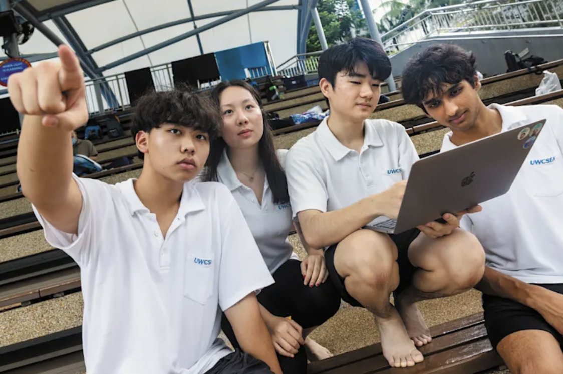 The team crouched on outdoor steps around a laptop, one member pointing into the distance